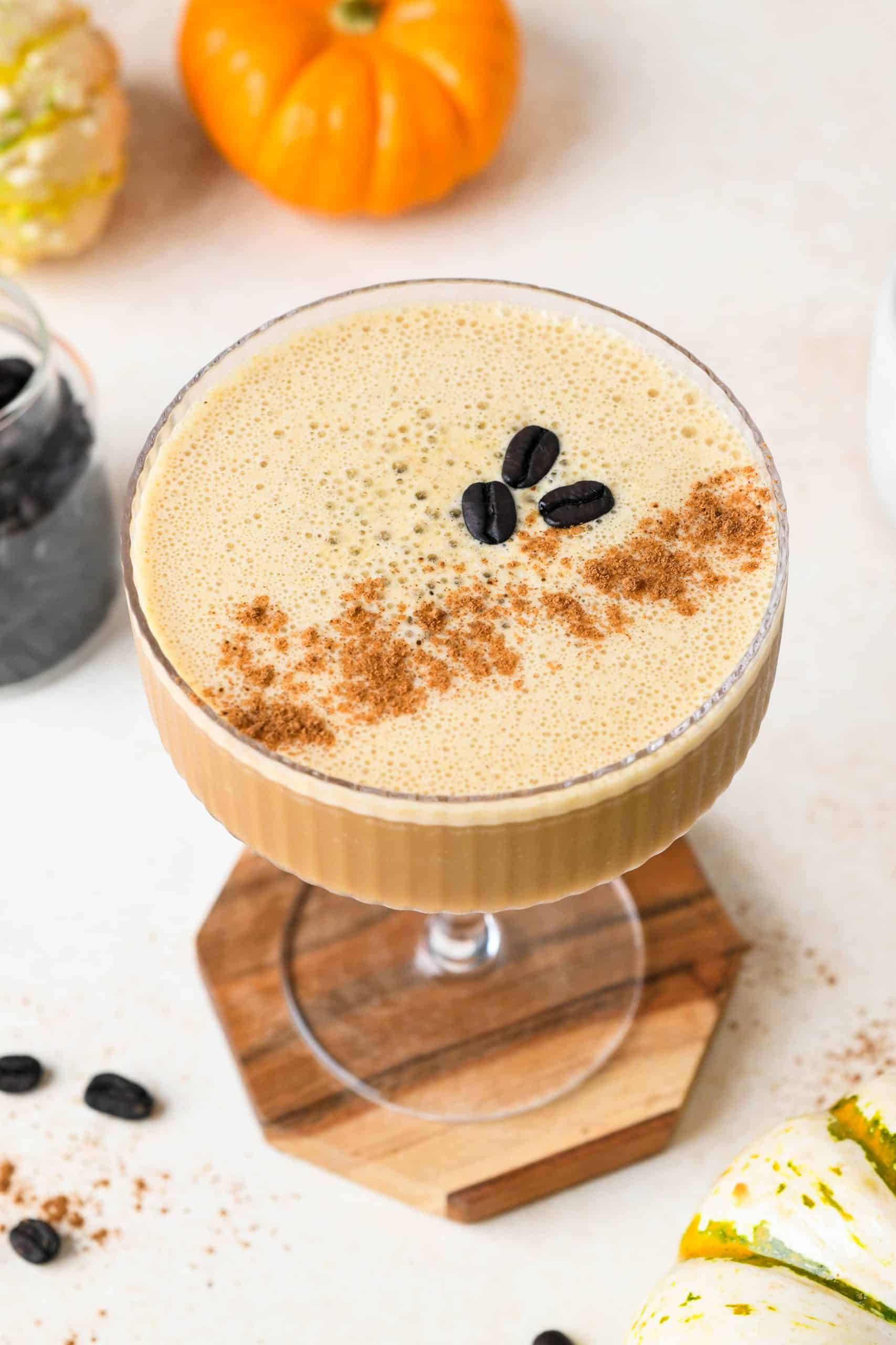 Overhead view of a creamy pumpkin spice espresso martini topped with 3 coffee beans and a dash of pumpkin pie spice, on a creamy background.
