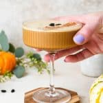 A pumpkin spice espresso martini on a coaster, with a hand reaching in to the image to pick it up.