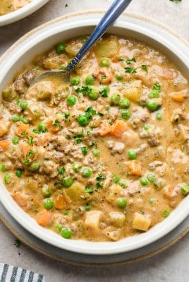 A bowl of thick and creamy shepherds pie soup, with a spoon tucked into the soup to show the creamy texture.