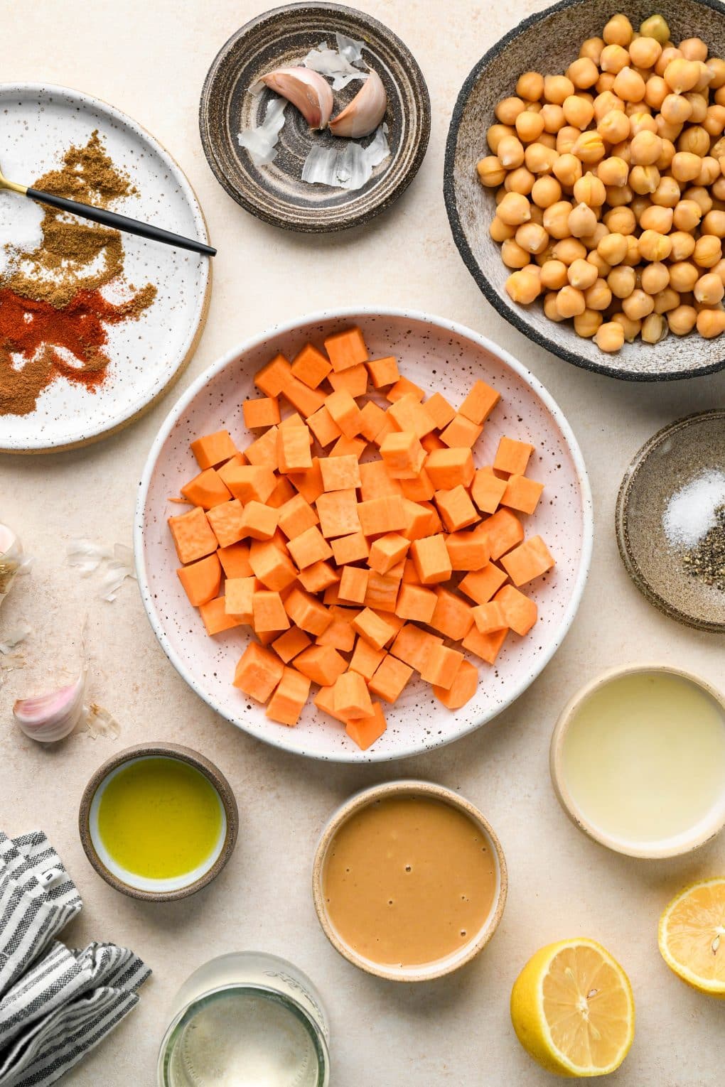 Ingredients for sweet potato hummus in various ceramics on a creamy colored background.