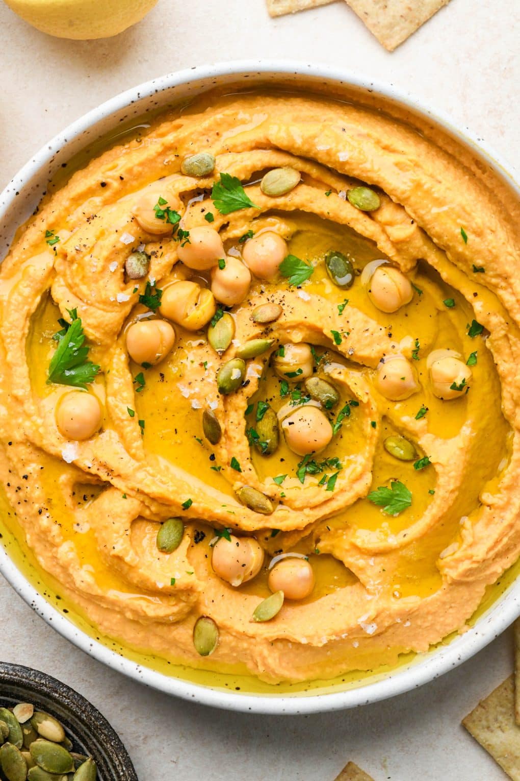 A shallow bowl of creamy sweet potato hummus topped with chickpeas, herbs, and pumpkin seeds.