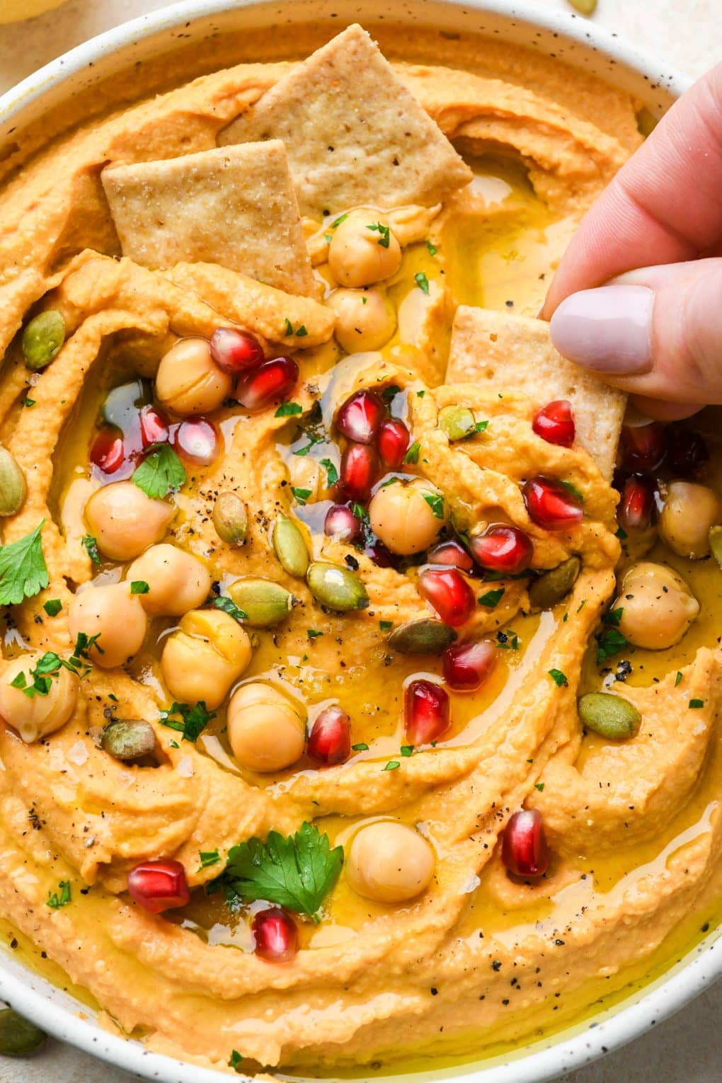 Close up image of a hand dipping a cracker into sweet potato hummus.