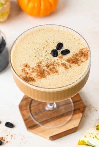 Overhead view of a creamy pumpkin spice espresso martini topped with 3 coffee beans and a dash of pumpkin pie spice, on a creamy background.