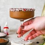 A peppermint mocha espresso martini in a martini glass with the rim lined with chocolate and peppermint candy.