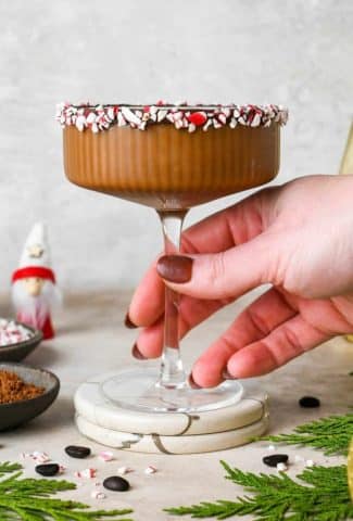 A peppermint mocha espresso martini in a martini glass with the rim lined with chocolate and peppermint candy.