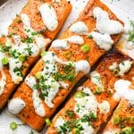 Four buffalo salmon filets on a white speckled plate baked to perfection and topped with a drizzle of dairy free ranch dressing, fresh herbs, and green onions.