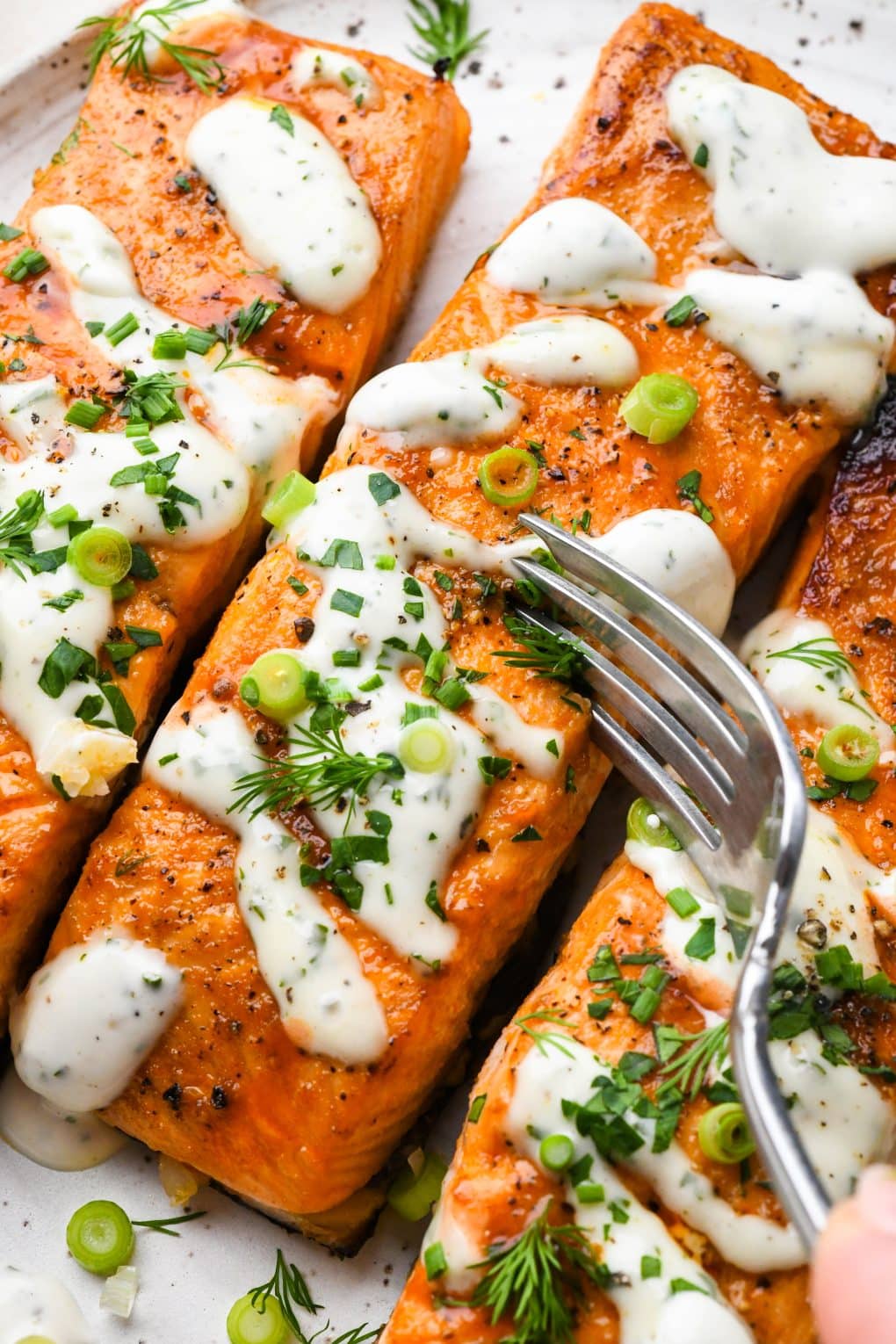A fork piecing into a buffalo salmon fillet that is topped with dairy free ranch dressing and fresh herbs.