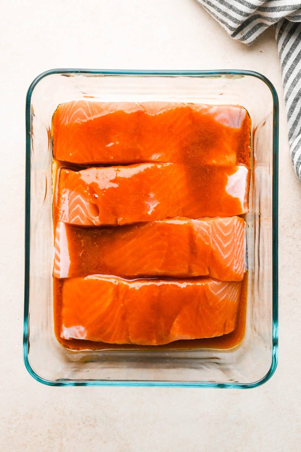 How to make baked buffalo salmon: Buffalo sauce poured over salmon fillets in a glass tupperware.