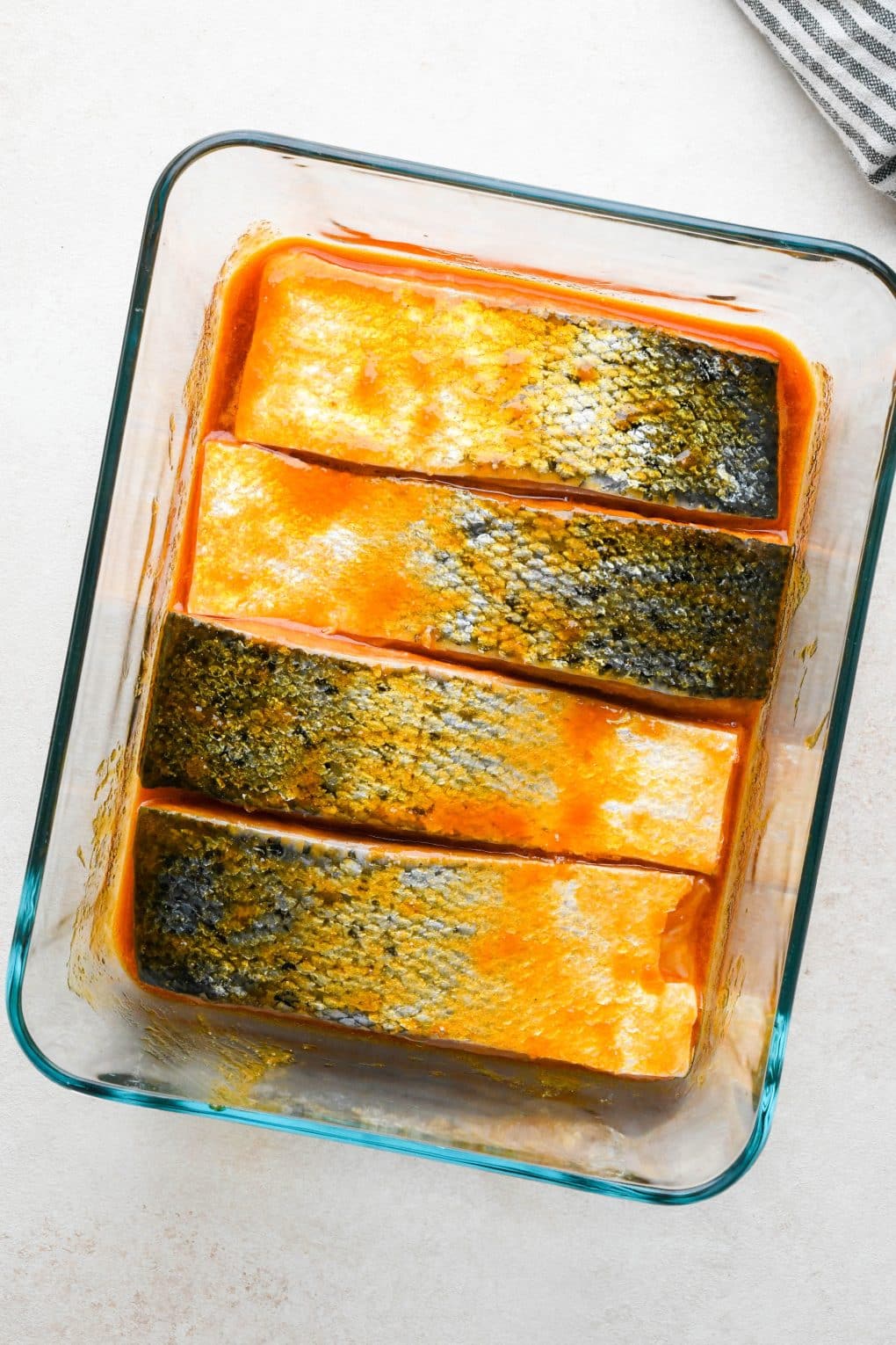 How to make baked buffalo salmon: Salmon fillets marinating in buffalo sauce in glass tupperware.
