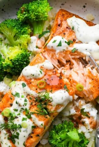 Close up image of a fork digging into a flaky and tender buffalo salmon fillet that's in a bowl with cauliflower rice and steamed broccoli.