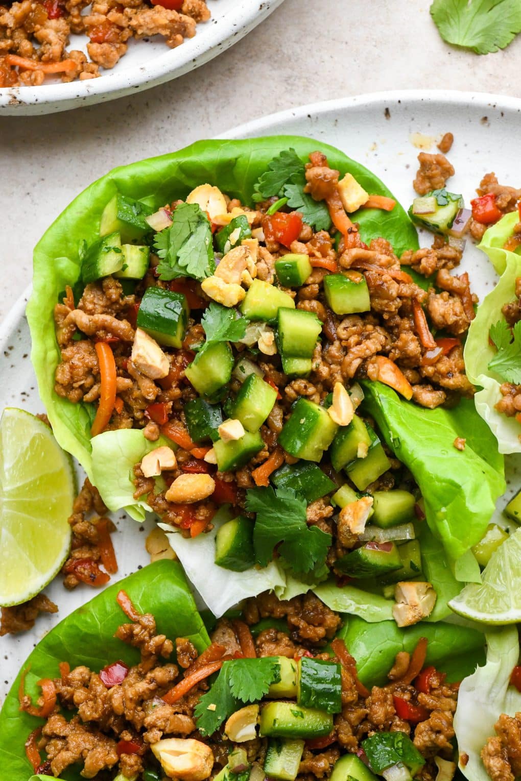 A single lettuce wrap on a large plate, topped with diced asian cucumber salad, chopped cashews, fresh cilantro, and lime wedges.