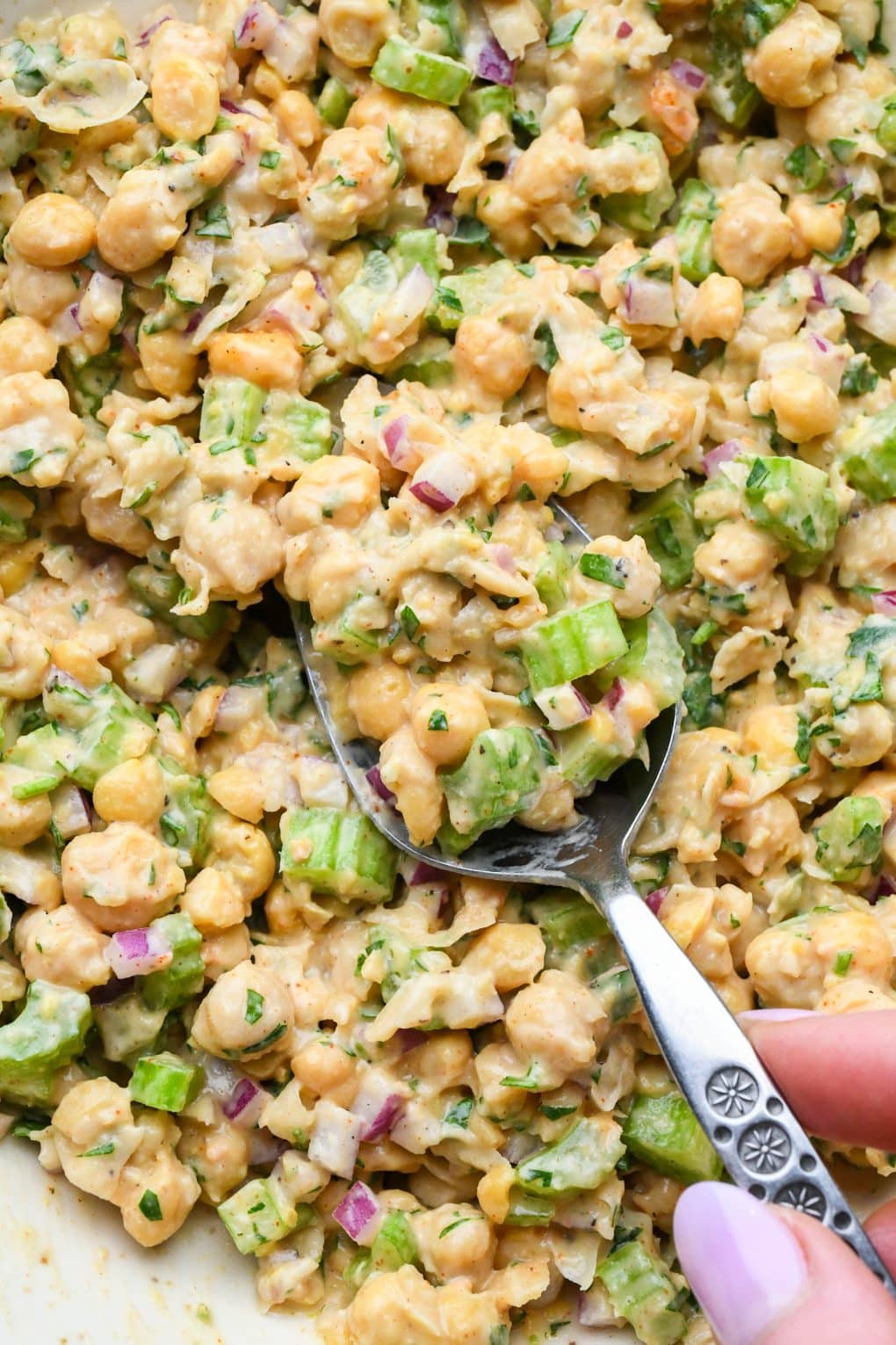 How to make smashed chickpea salad: Close up of a mixing spoon full of chickpea salad to show the creamy chunky texture.