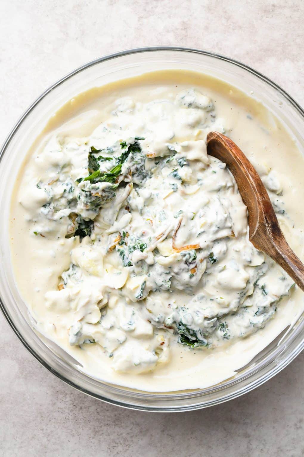 How to make Dairy Free Spinach Artichoke Dip: A wooden spoon mixing cashew cream into the other dip ingredients.