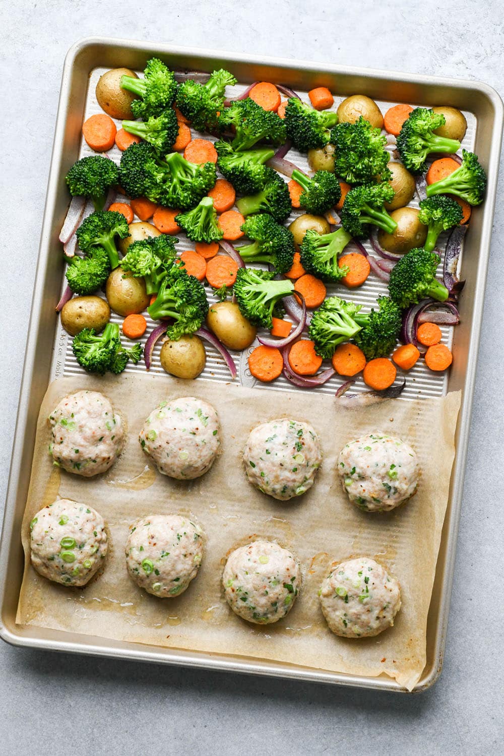 How to make Roasted Veggie Protein Bowls with Turmeric Tahini: Sheet pan with chicken patties and veggies partially baked, raw broccoli florets added to the veggie side of the sheet pan.