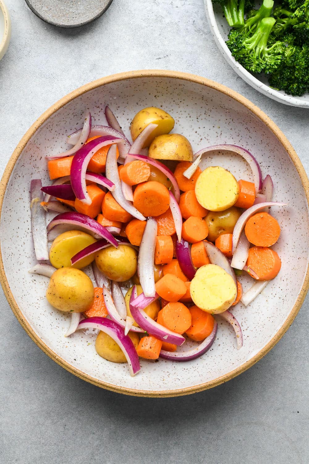 How to make Roasted Veggie Protein Bowls with Turmeric Tahini: Carrots, onions, and potatoes in a large ceramic bowl with broccoli florets on a plate on the side.