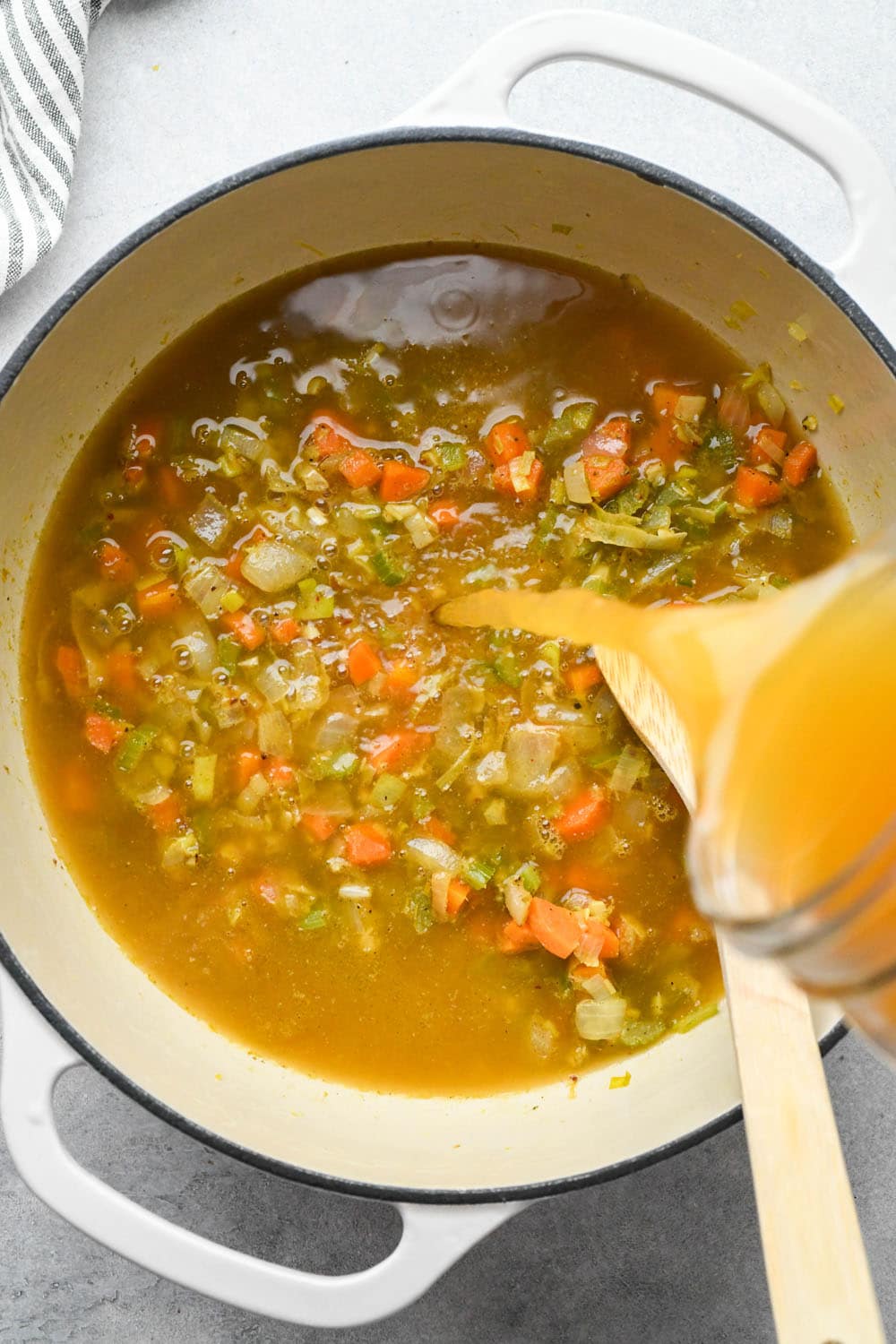How to make White Bean and Kale Soup: Pouring broth into soup pot with veggies and spices.