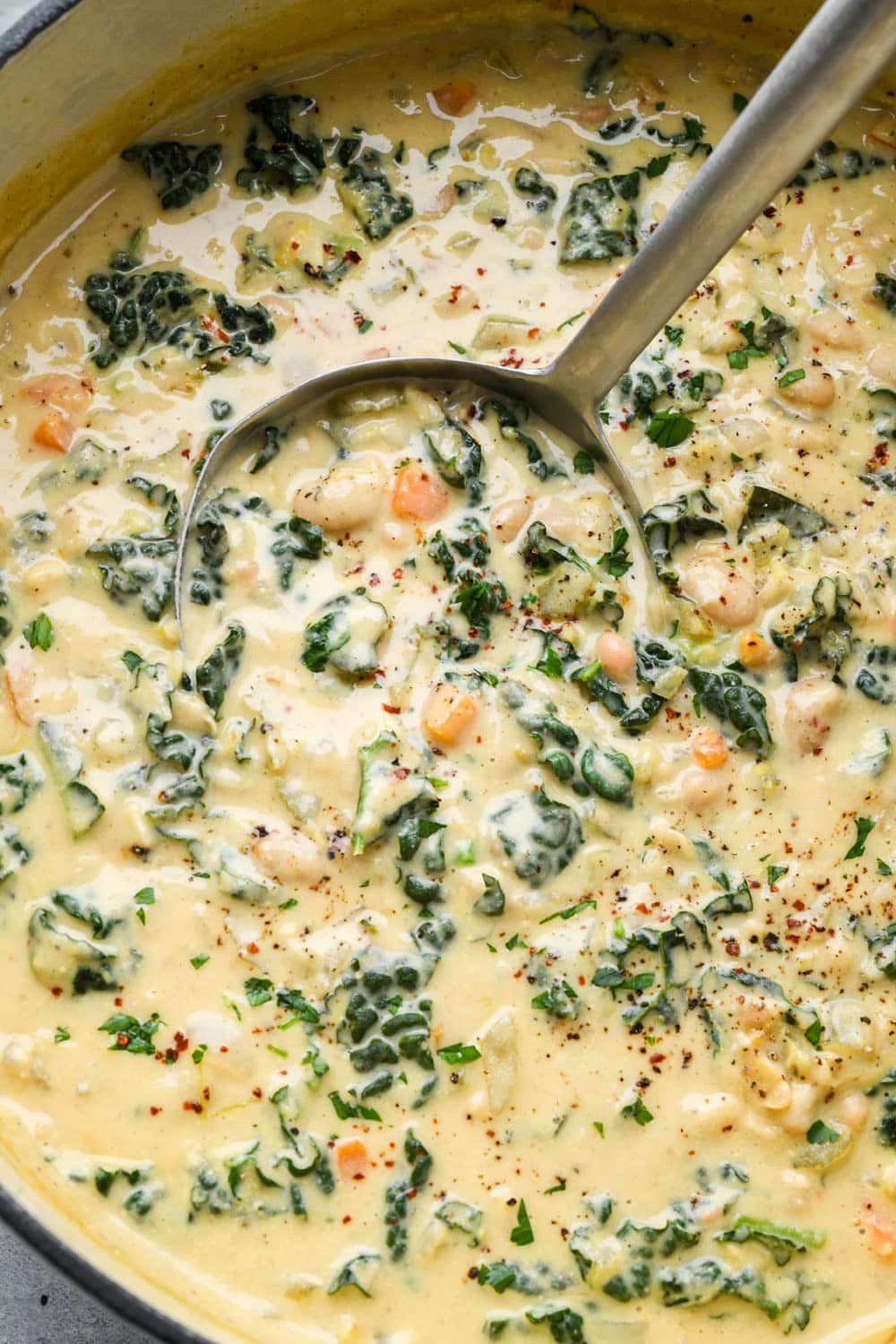 A ladle lifting out a portion of creamy dairy free white bean and kale soup from a large white soup pot.