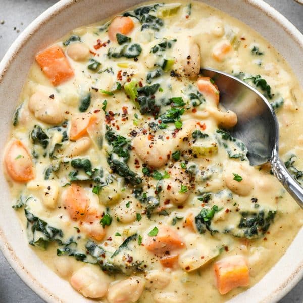 A creamy ceramic bowl of creamy white bean and kale soup with a soup spoon dipping into the bowl for a bite.