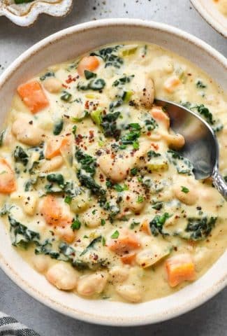 A creamy ceramic bowl of creamy white bean and kale soup with a soup spoon dipping into the bowl for a bite.