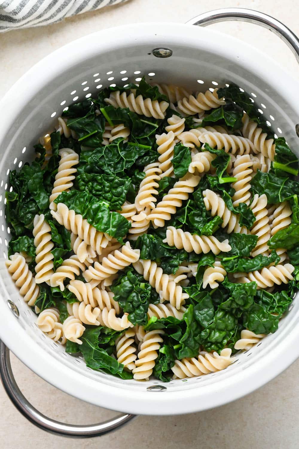 How to make Creamy Tomato Sausage Pasta: Cooked pasta and kale drained in a white metal colander.