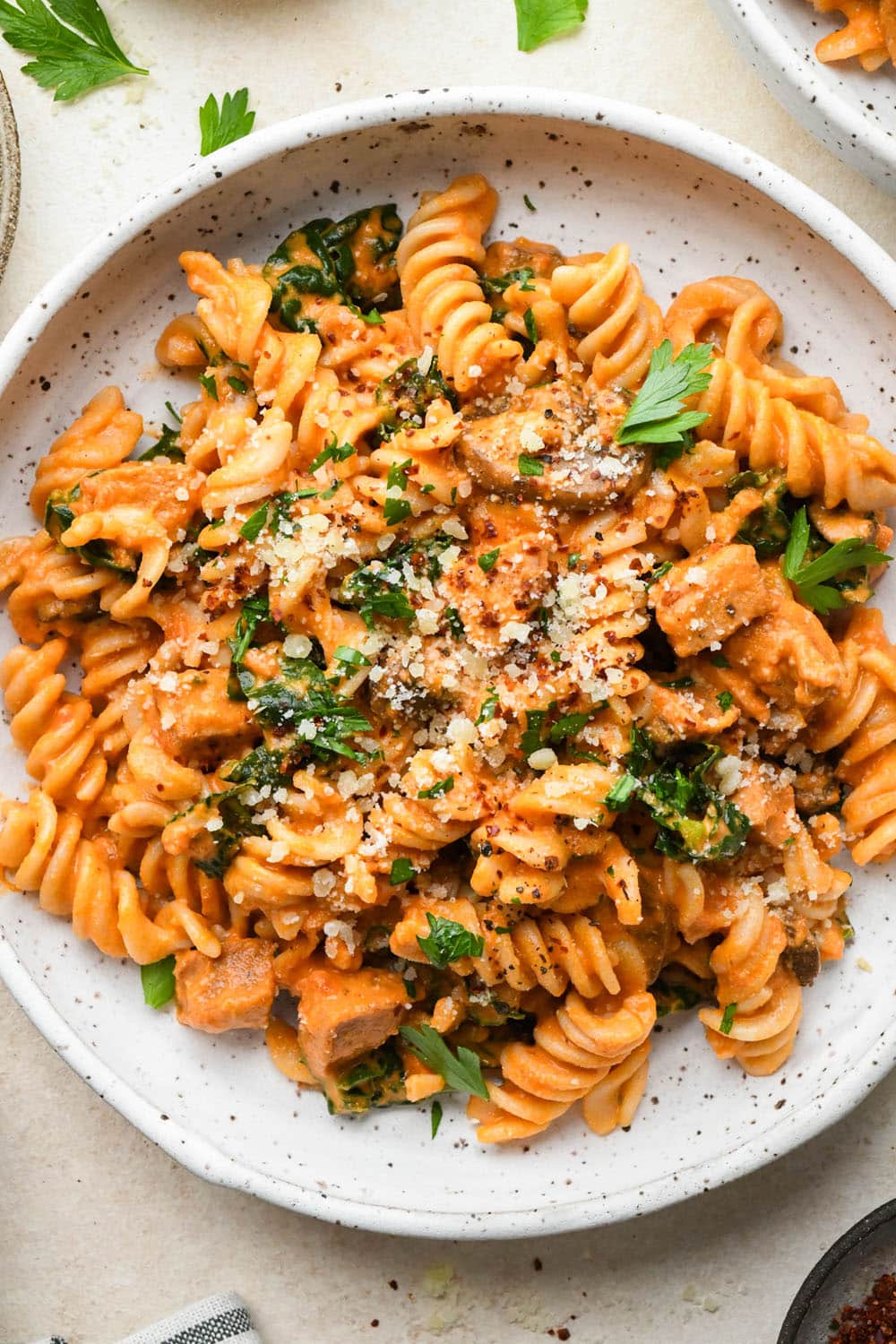How to make Creamy Tomato Sausage Pasta: Pasta in a shallow ceramic bowl, topped with dairy free parmesan and fresh herbs.