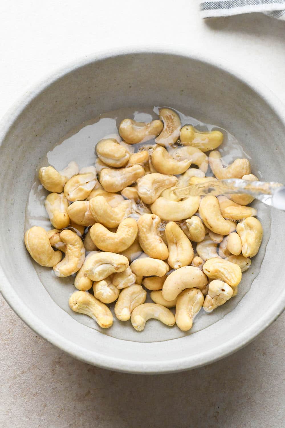 How to make Creamy Tomato Sausage Pasta: Pouring hot water over raw cashews in a grey ceramic bowl.