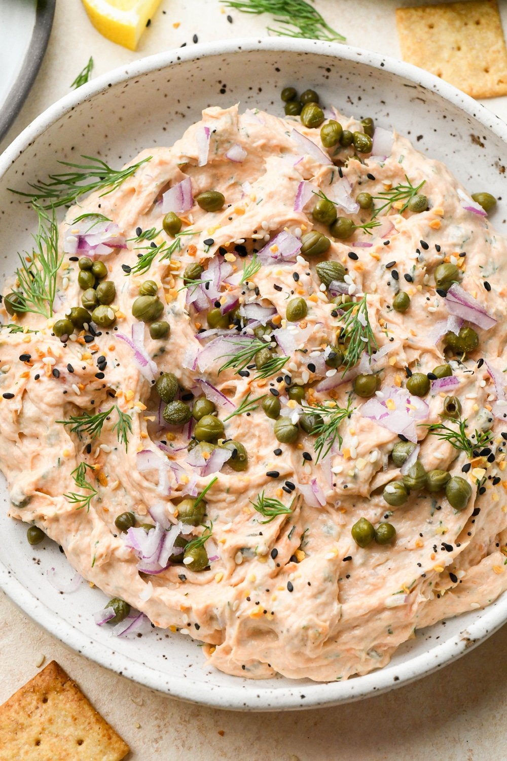Dairy free smoked salmon dip in a small shallow ceramic speckled bowl, garnished with capers, fresh dill, everything but the bagel seasoning.