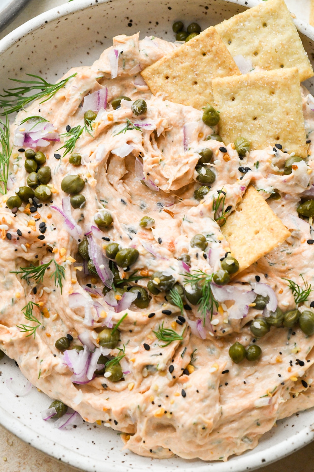Dairy free smoked salmon dip in a shallow bowl topped with garnishes, after a cracker has scooped some of the dip out of the bowl.