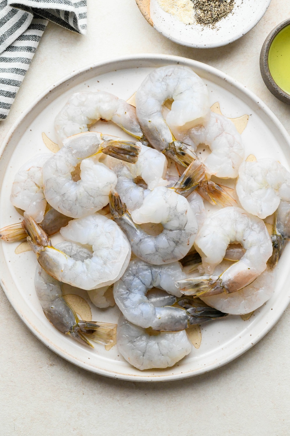 Ingredients for pan seared shrimp on various ceramics on a cream colored background, next to a blue and white striped napkin.