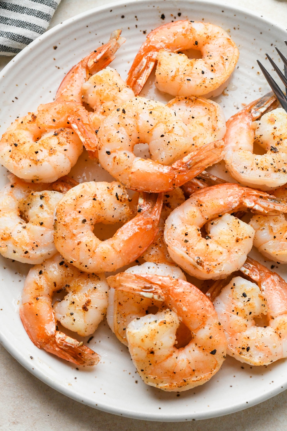 Pan seared shrimp on a large speckled white plate next to a striped napkin.
