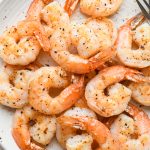 Pan seared shrimp on a large speckled white plate next to a striped napkin.