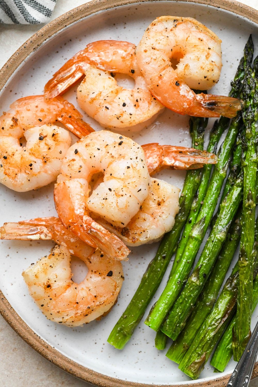 Six pan seared shrimp on a ceramic plate with roasted asparagusl