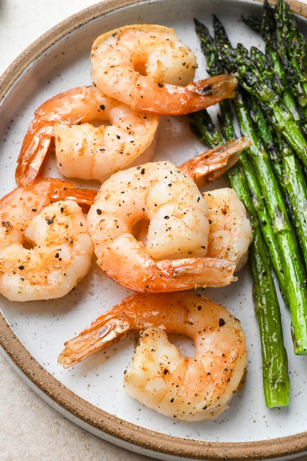 Six pan seared shrimp on a ceramic plate with roasted asparagus.