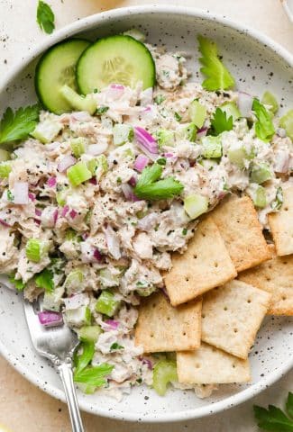 Healthy tuna salad in a bowl with sliced cucumber and gluten free crackers.