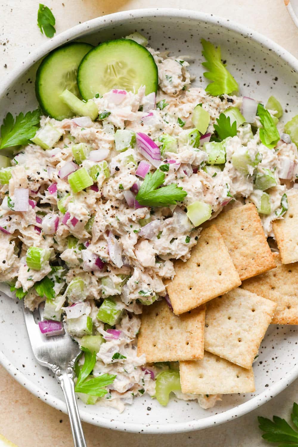 Healthy tuna salad in a bowl with sliced cucumber and gluten free crackers.
