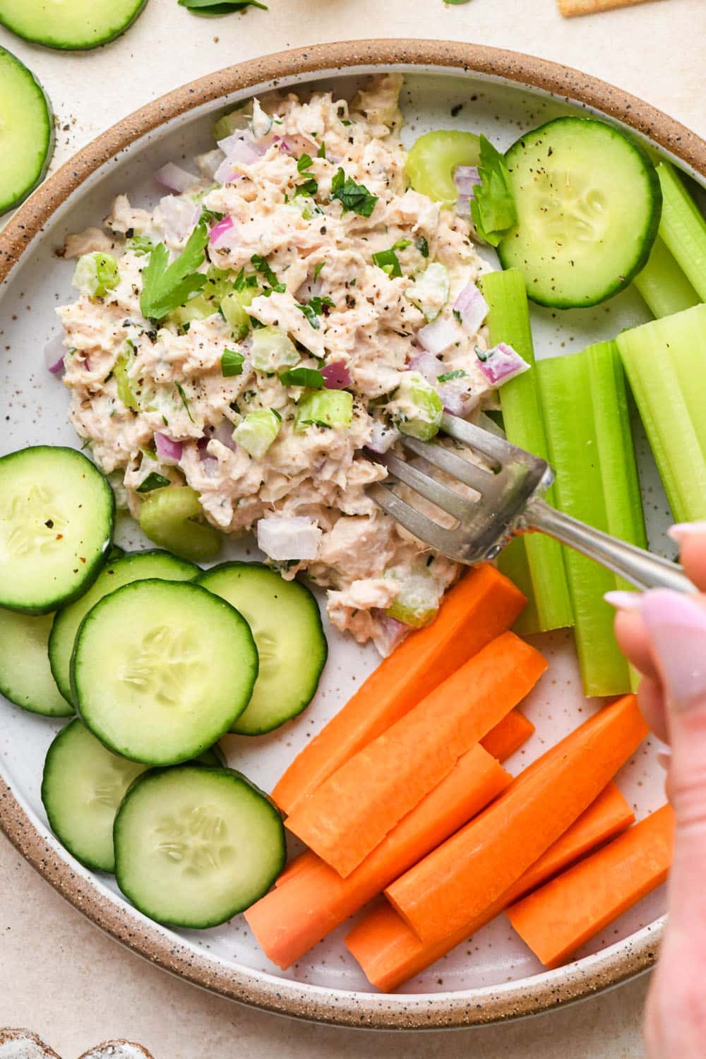 A scoop of healthy tuna salad on a plate with cut veggies and a fork digging into the tuna salad.