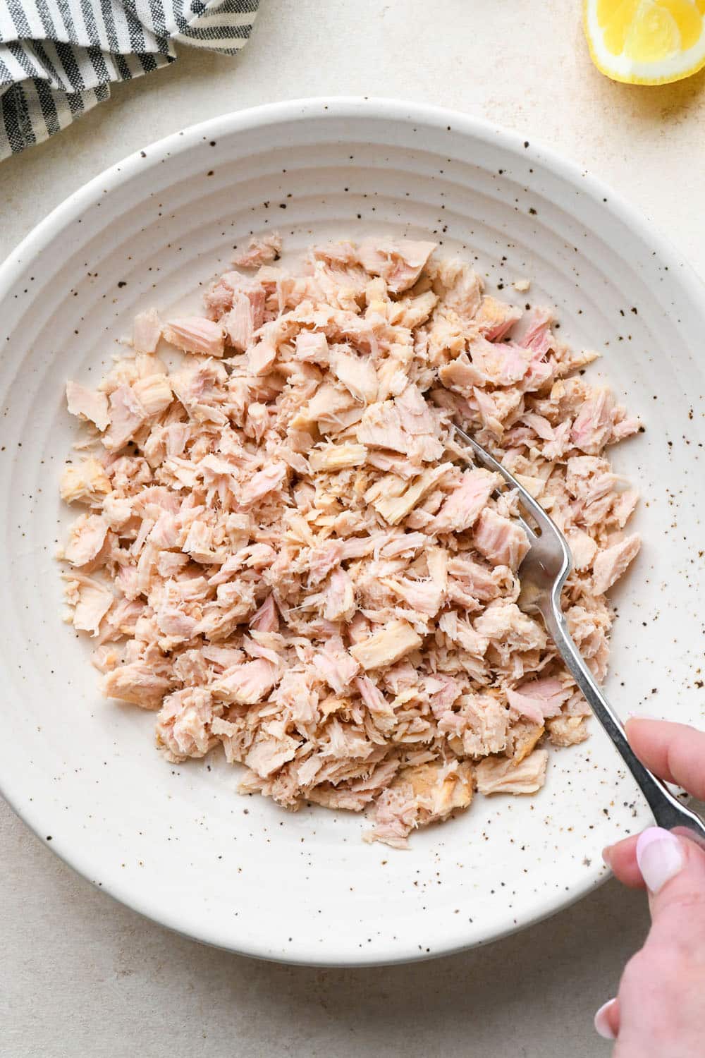 How to make tuna salad: Drained tuna added to a large bowl and flaked apart with a fork.