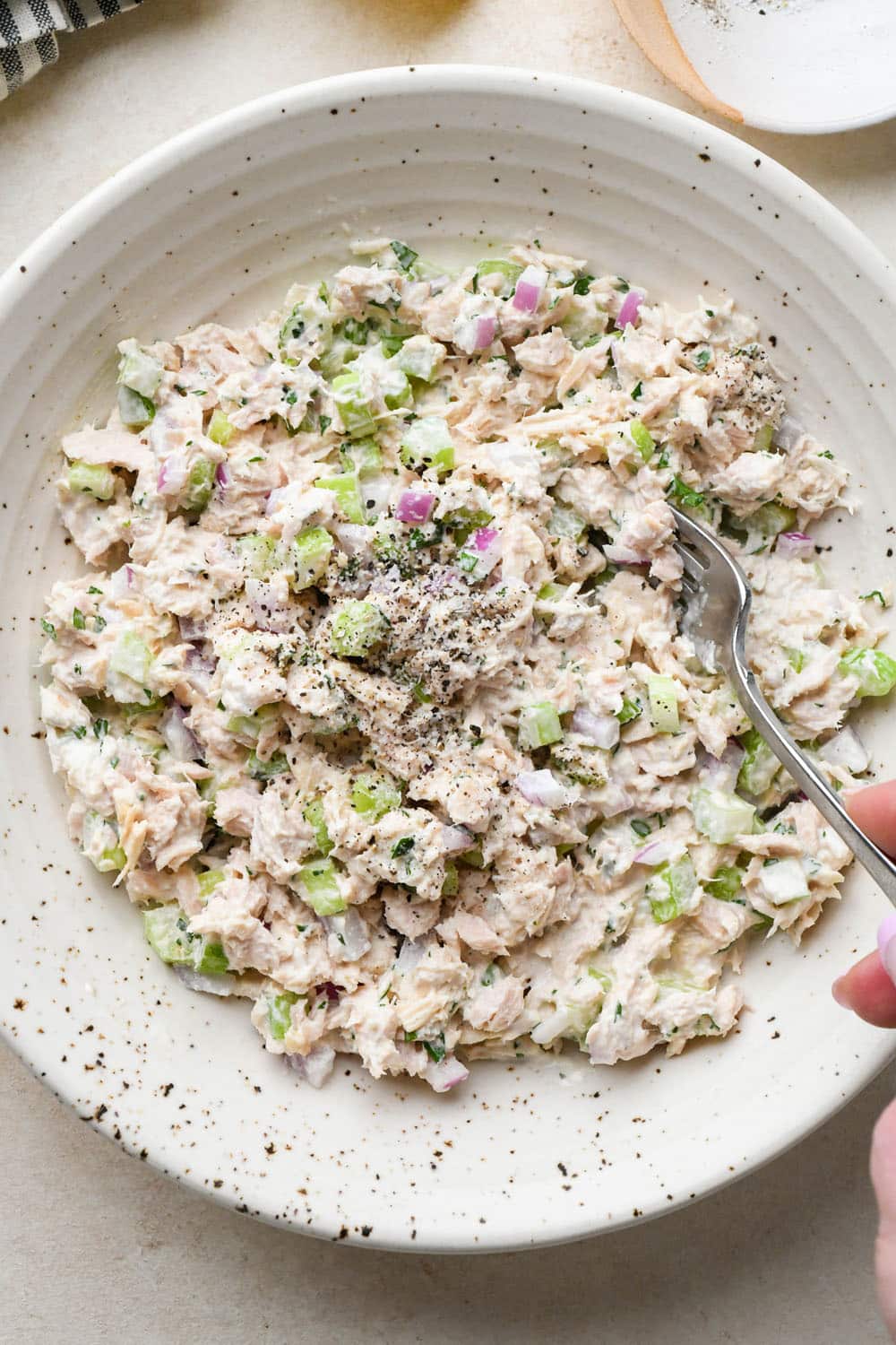 How to make tuna salad: All ingredients for tuna salad mixed together in a large bowl, seasoned with salt and pepper.