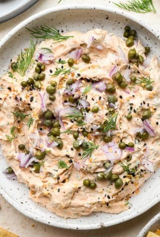 Dairy free smoked salmon dip in a small shallow ceramic speckled bowl, garnished with capers, fresh dill, everything but the bagel seasoning.