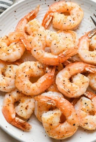 Pan seared shrimp on a large speckled white plate next to a striped napkin.