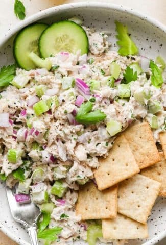 Healthy tuna salad in a bowl with sliced cucumber and gluten free crackers.