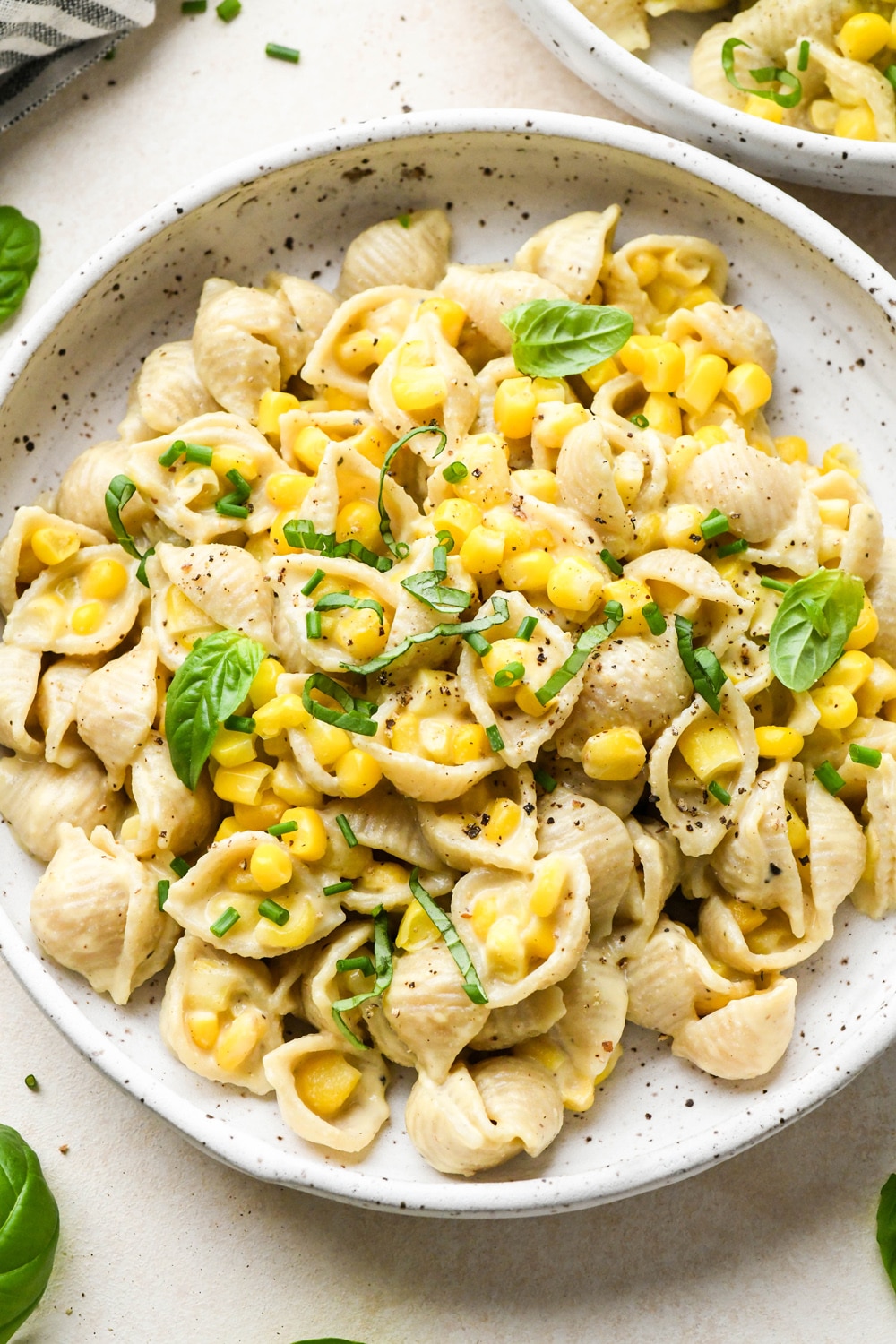 A shallow white speckled pottery bowl with creamy dairy free corn pasta topped with fresh basil and fresh chives.