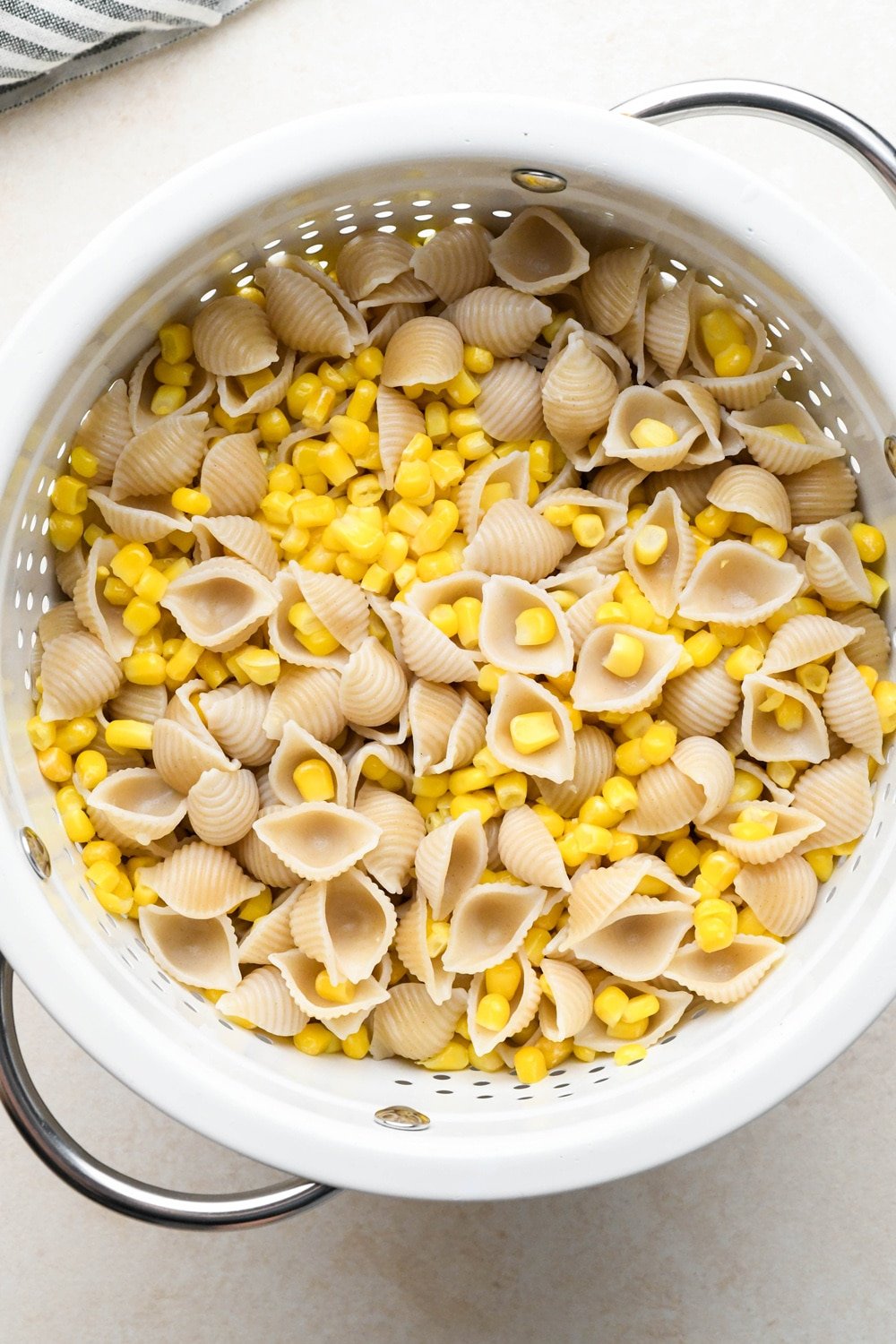 How to make Creamy Dairy Free Corn Pasta with Basil: Cooked pasta and corn drained in a white colander. 