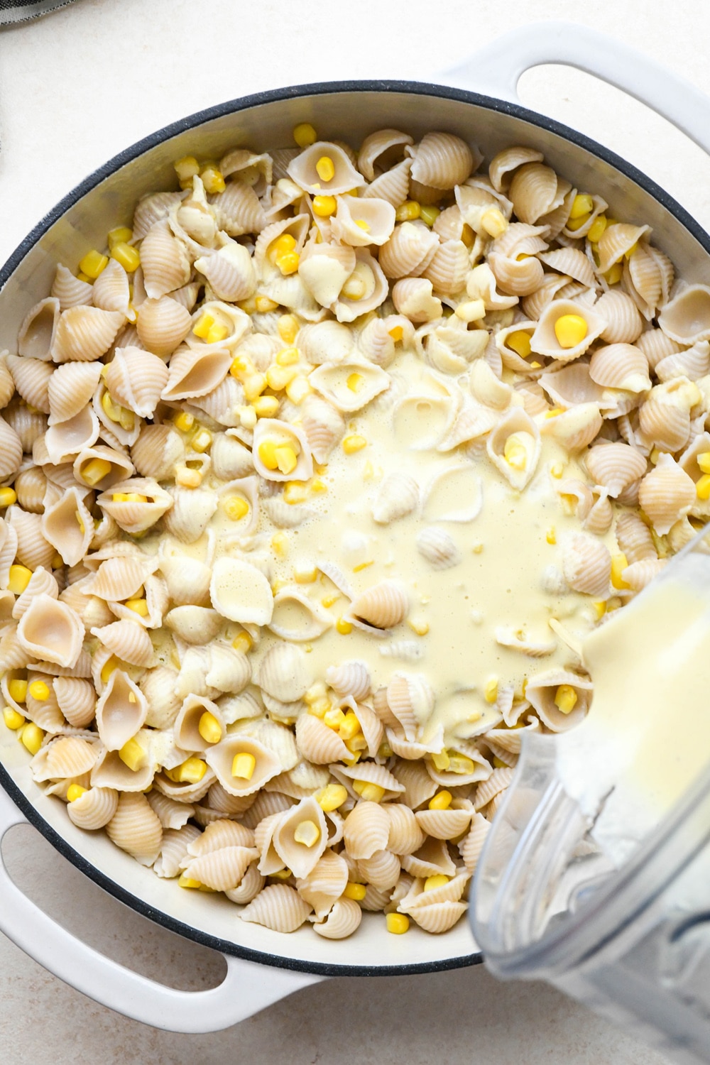 How to make Creamy Dairy Free Corn Pasta with Basil: Pouring cashew cream sauce into skillet with pasta and corn from blender container.
