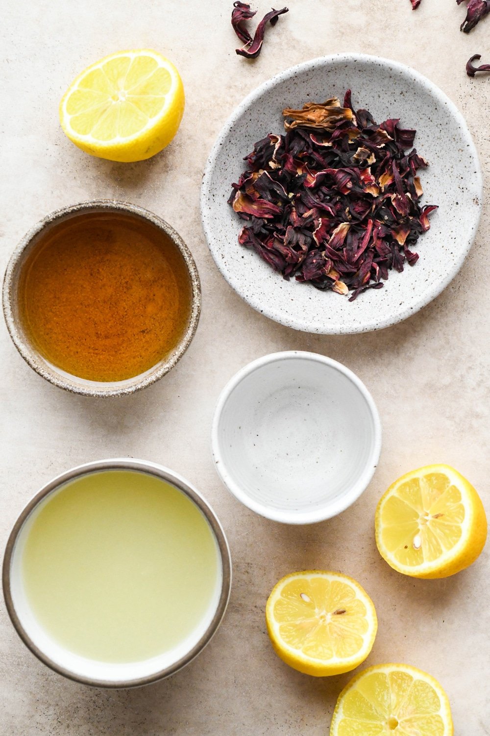 Ingredients to make hibiscus lemonade in various ceramics on a creamy colored background.