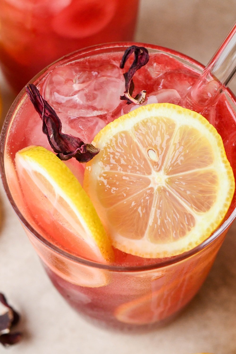 Overhead shot of a glass of hibiscus lemonade, topped with lemon wheels and dried hibiscus flowers.