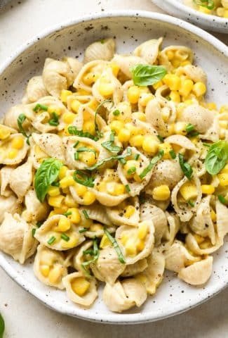 A shallow white speckled pottery bowl with creamy dairy free corn pasta topped with fresh basil and fresh chives.