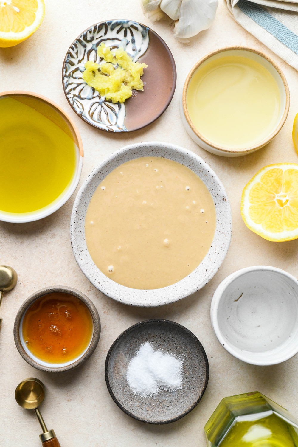 Ingredients for tahini dressing in various ceramics on a light cream colored background.