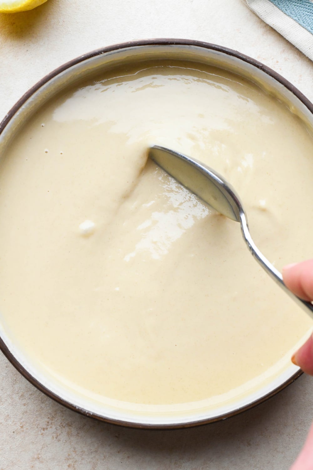 How to make tahini dressing: A spoon moving through the bowl of tahini dressing to show the texture.