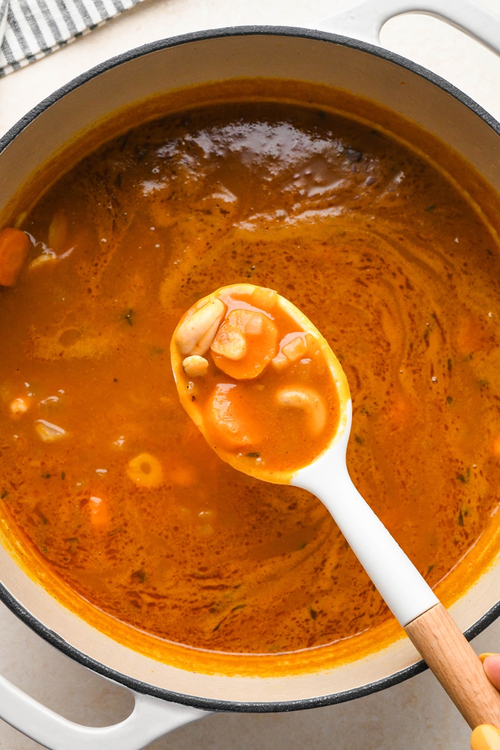How to make Dairy Free Pumpkin Carrot Soup: A spoon lifting out some of the cashews and carrots from the soup after simmering to show the texture of the plump cashews.